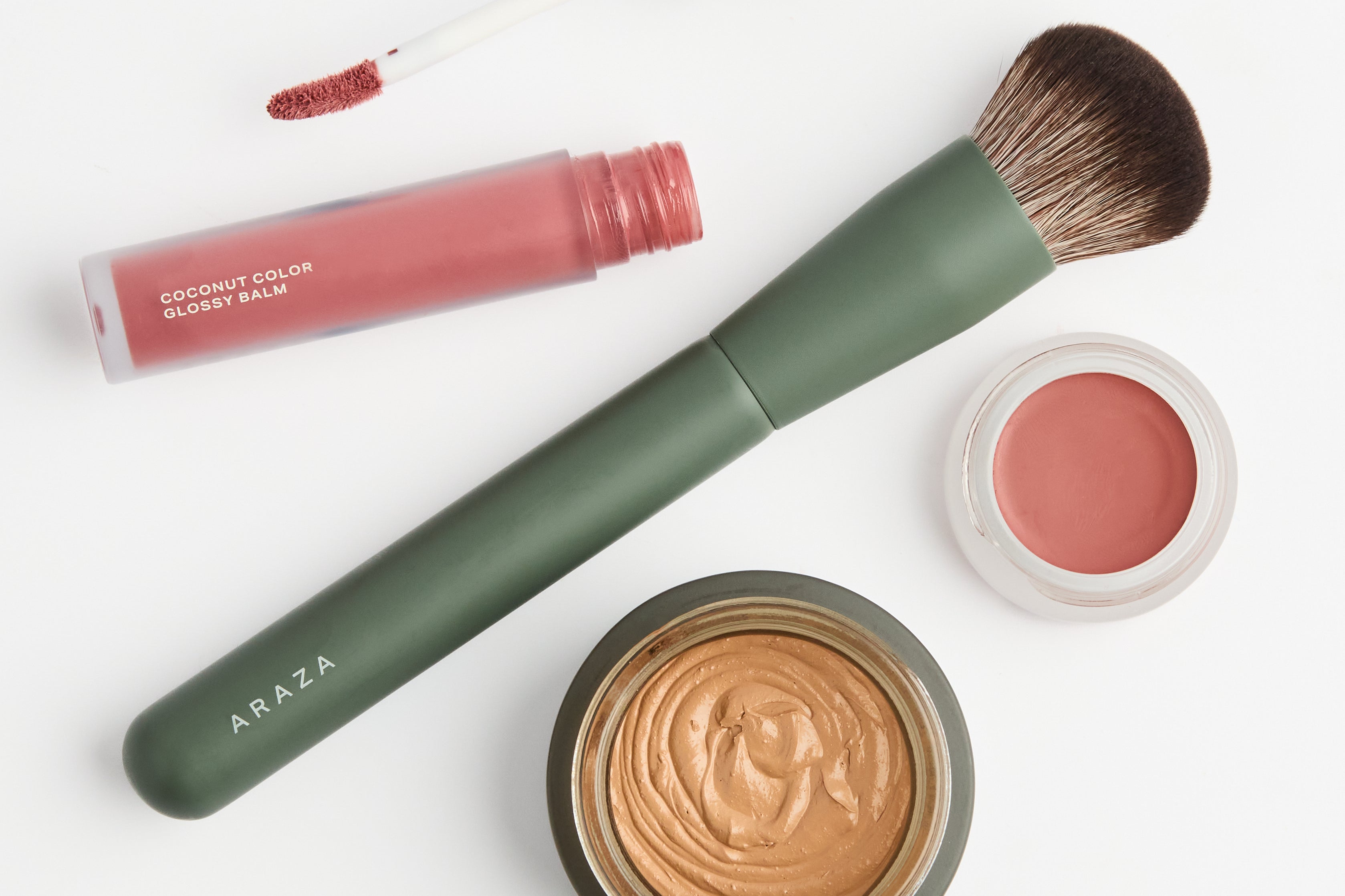 overhead shot of Coconut Cream Foundation,
Blending Brush,
Mango Cream Color Pot, and 
Coconut Color Glossy Balm scattered on a white background