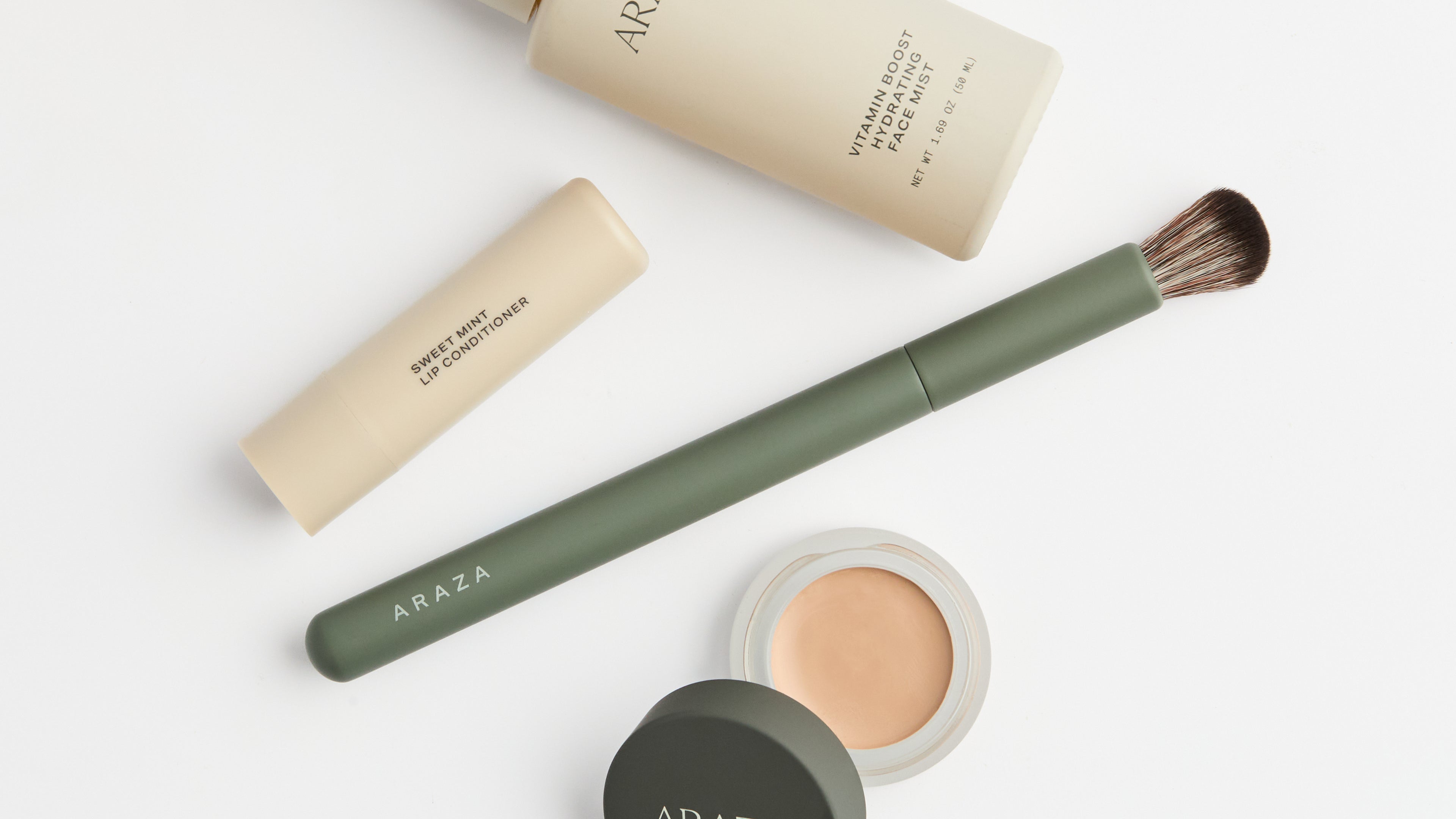 overhead shot of an open coconut cream concealer, sweet mint lip conditioner, the small blending brush, and the vitamin boost hydrating face mist against a white background