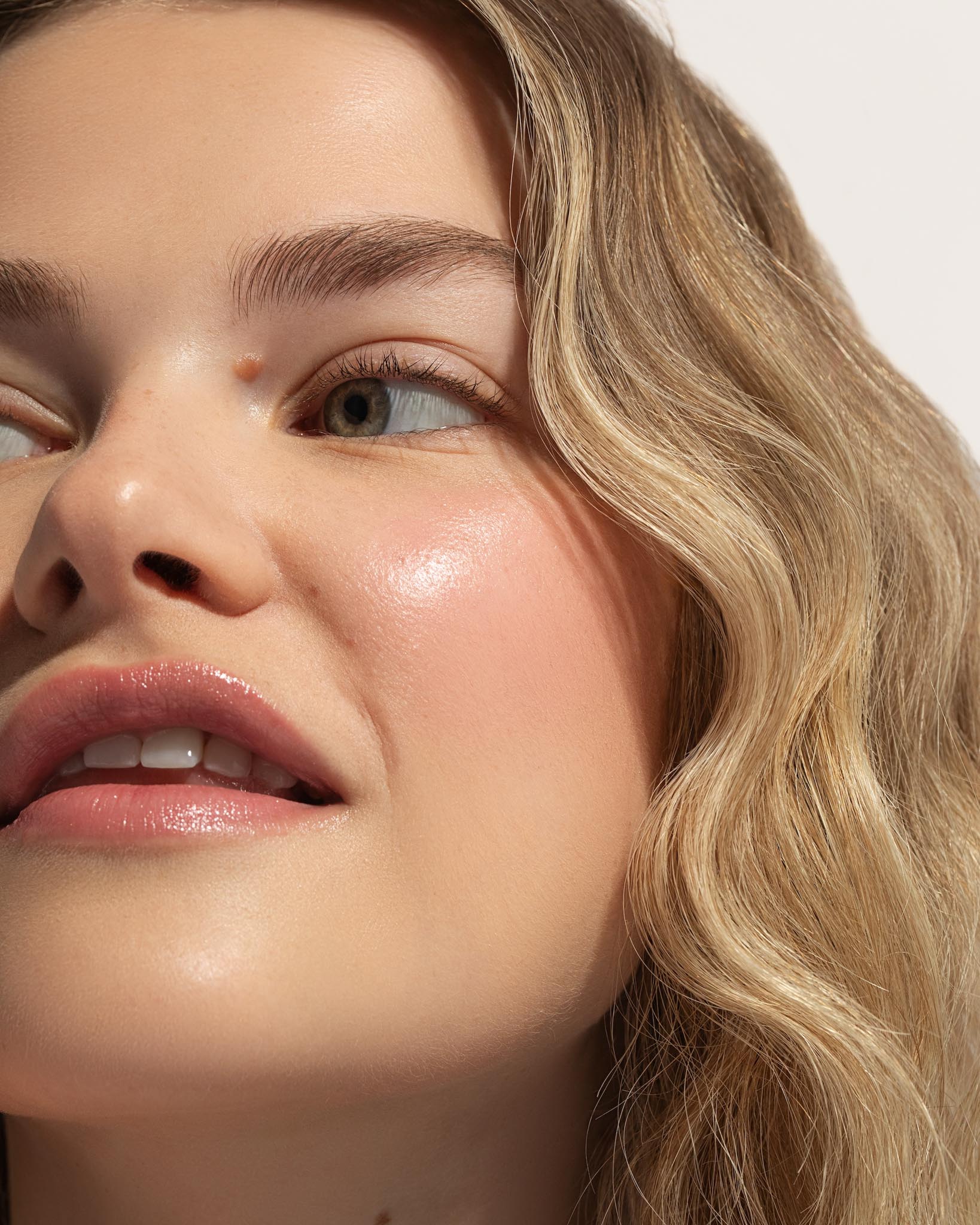 Close-up of a woman's face with blonde hair and pink lips on a neutral background