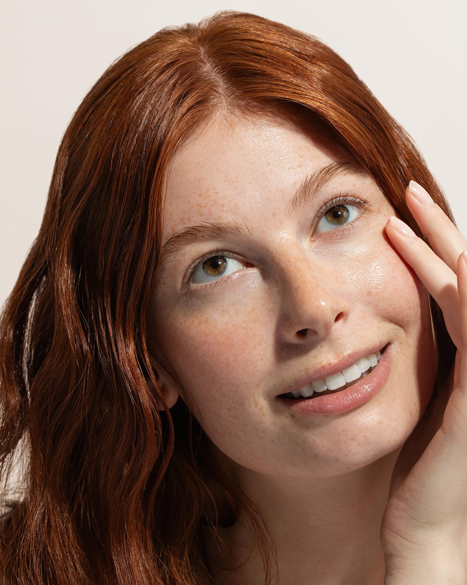 Woman with red hair touching her face against a neutral background