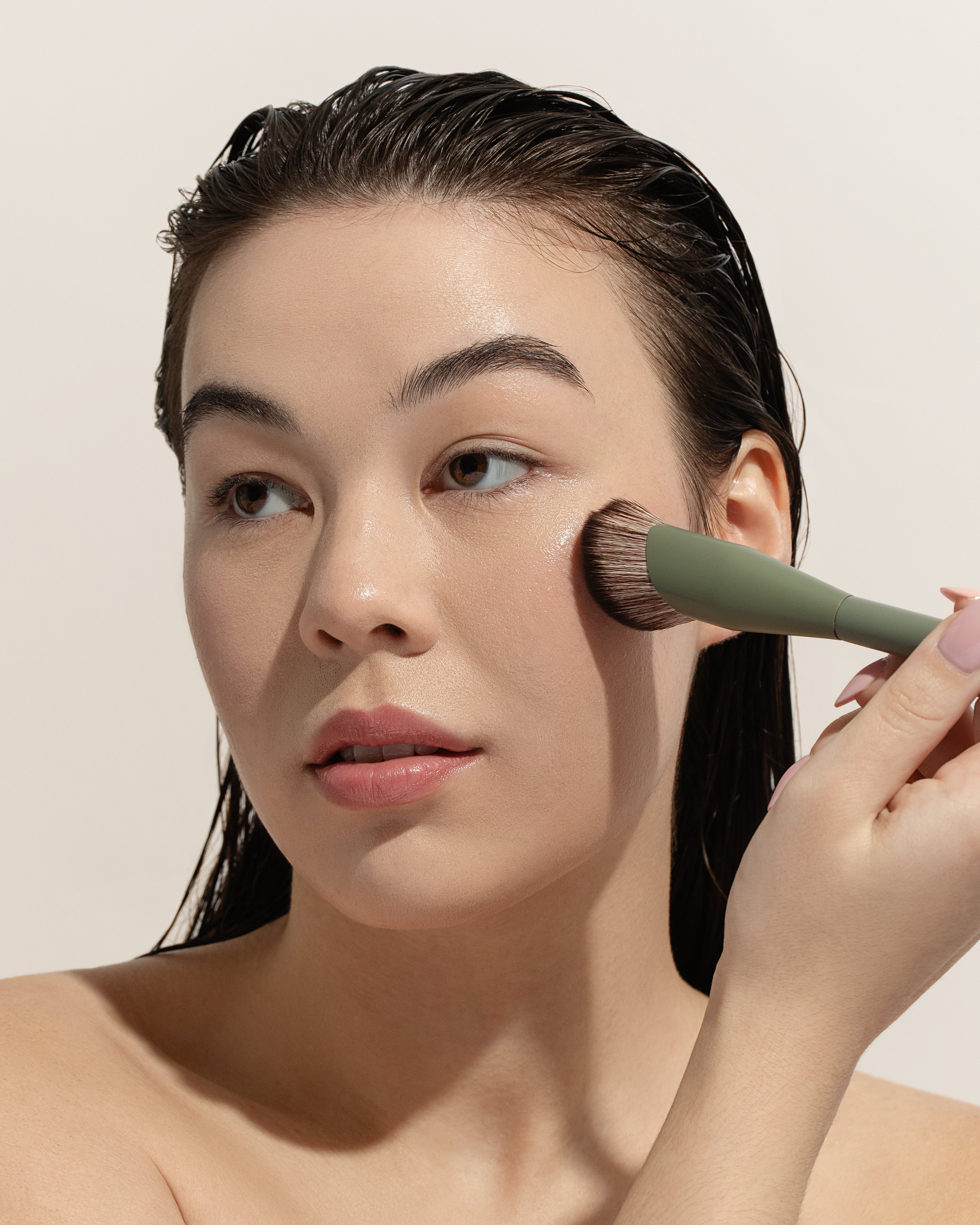 Woman applying makeup with a brush on a beige background