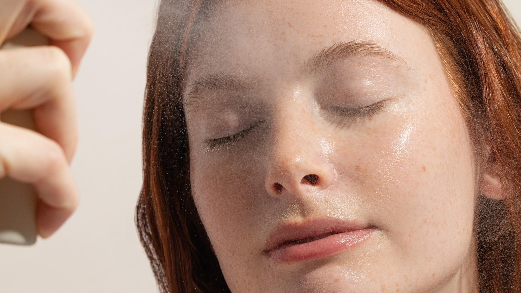 Person applying the vitamin boost hydrating face mist to their face with a neutral background