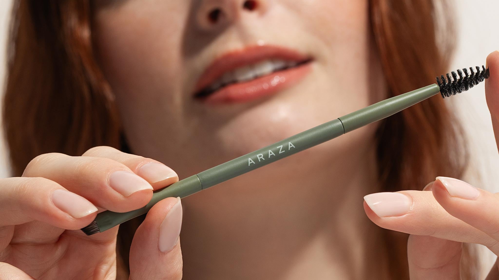 Person holding a green ARAZA brow brush to the camera